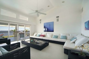A modern living room with a large sofa, a coffee table, and a view of the sea. - CCVS – Villa Southern Living (Cape Coral)