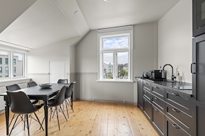 A modern kitchen with a dining area, wooden flooring, and a view of buildings through the window. - Best View in Downtown Reykjavik! 3 Bedrooms + 3 Ensuite-Bathrooms (Reykjavík)