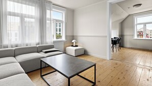 Ein modernes Wohnzimmer mit einer Eckcouch, einem kleinen Tisch und einem Essbereich mit Stühlen.