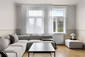 A modern living room with a grey sofa, a small table, and a window with sheer curtains. - Best View in Downtown Reykjavik!  3 Bedrooms + 3 Ensuite-Bathrooms (Reykjavík)