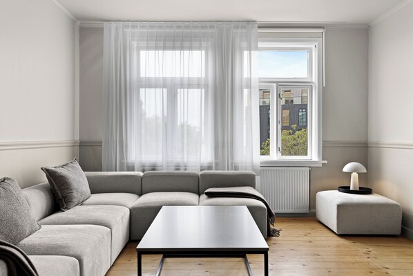 A modern living room with a grey sofa, a small table, and a window with sheer curtains. - Best View in Downtown Reykjavik! 3 Bedrooms + 3 Ensuite-Bathrooms (Reykjavík)