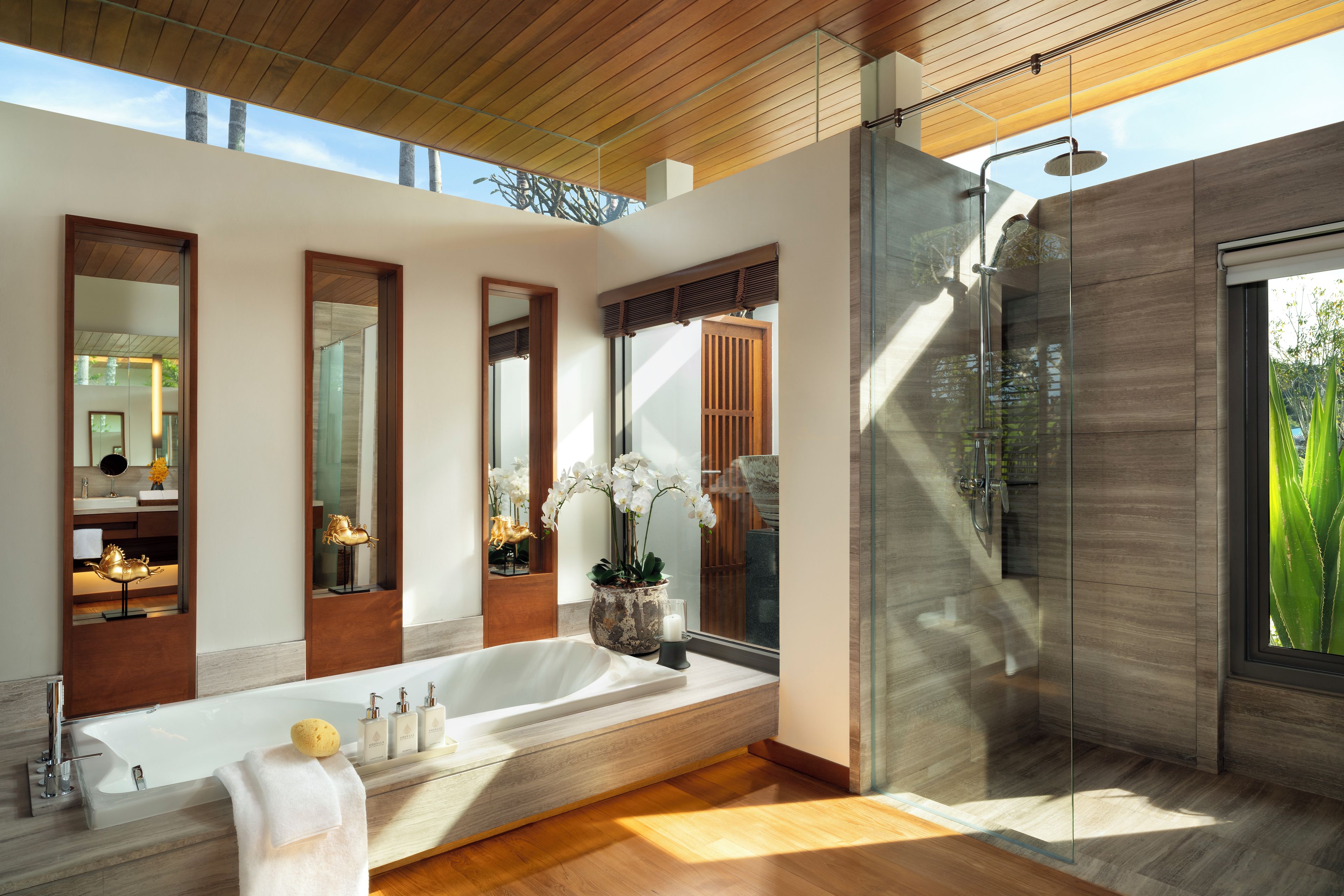 Un baño moderno con una bañera grande, una ducha con mampara de vidrio y varios espejos.