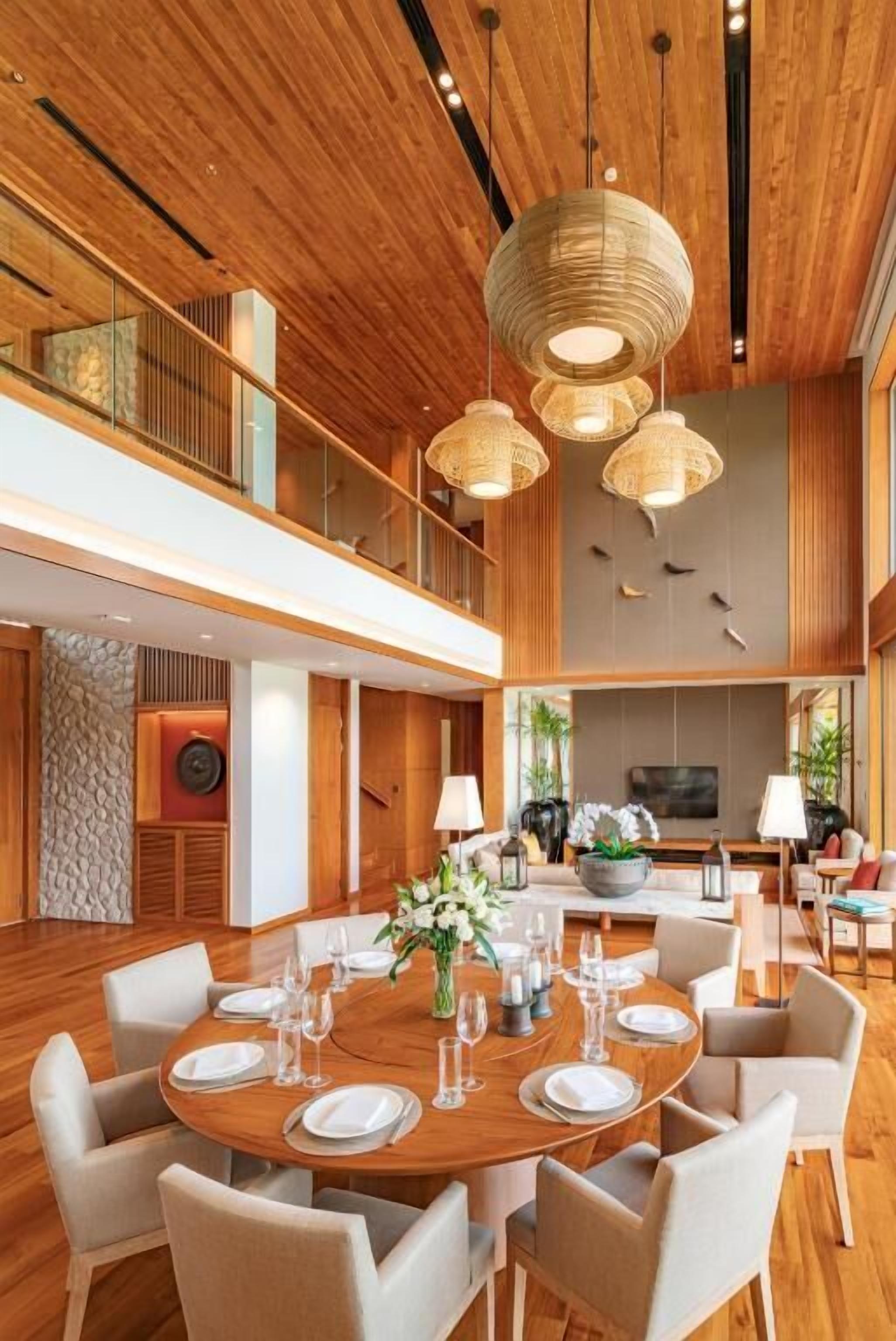 A spacious dining area with a round table set for six, surrounded by chairs, under a wooden ceiling with hanging light fixtures.