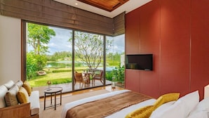 A bedroom with a large window, a bed, a TV, and a view of a garden.