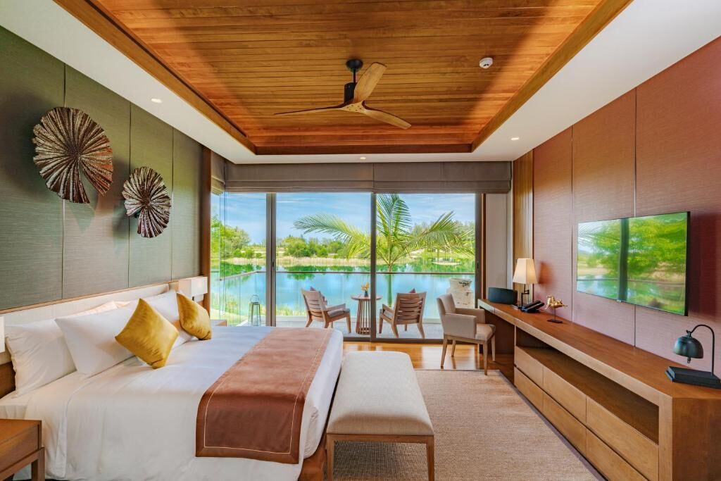 A modern hotel room with a bed, seating area, and a view of a body of water.