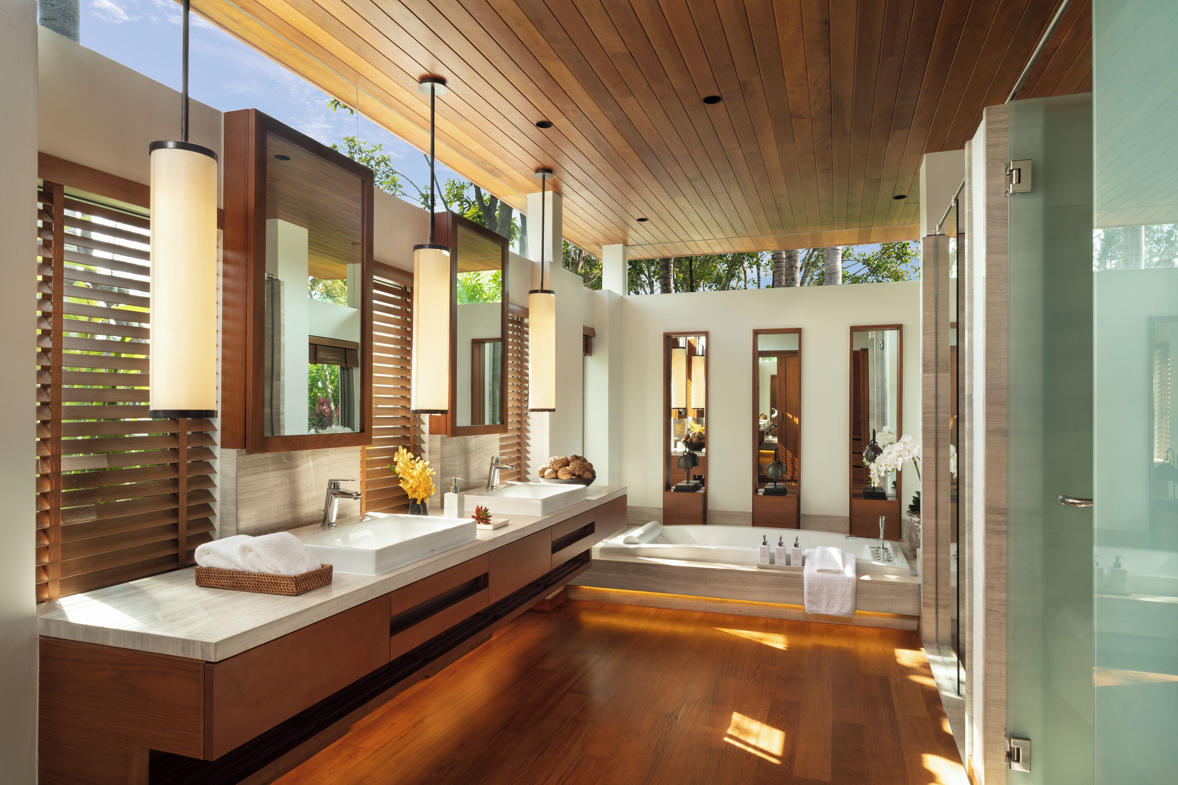 Un baño moderno con suelo de madera, lavamanos dobles y espejos grandes.