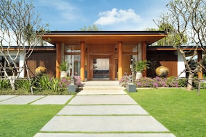 Un bâtiment moderne doté d’une entrée couverte, d’une façade en pierre et d’un jardin bien entretenu, avec des pierres plates qui servent de chemin menant à la porte.