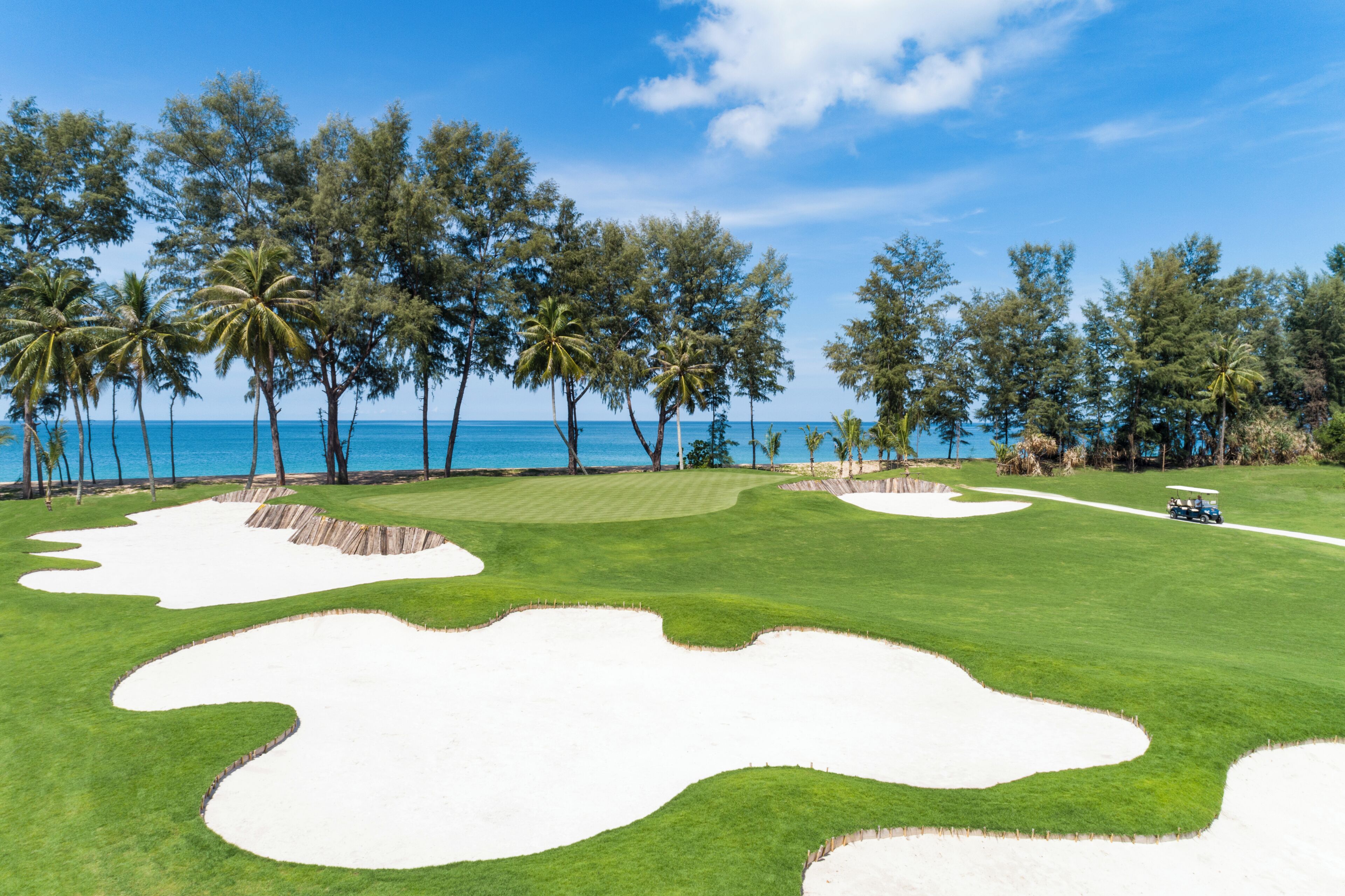 A golf course with sand bunkers, a clear sky, and a view of the ocean.