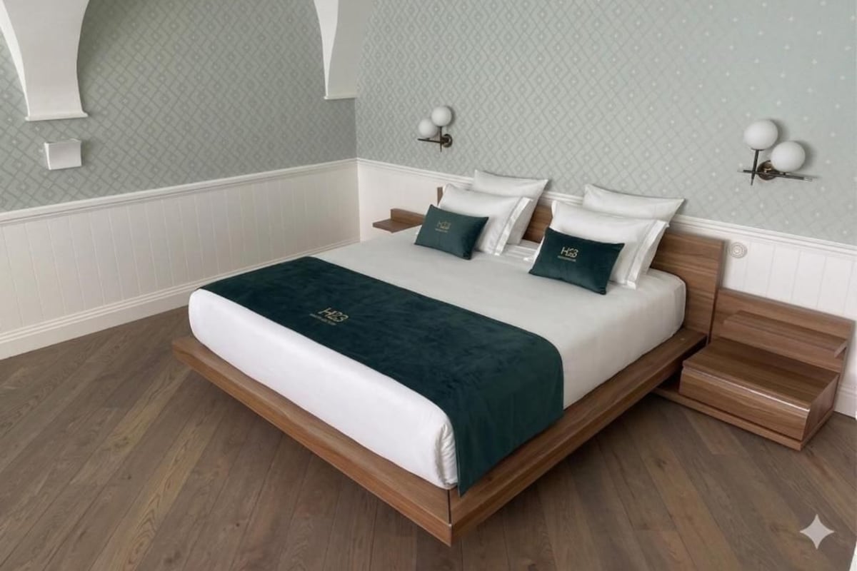 Un letto rifatto con cura, con una coperta e dei cuscini verde scuro abbinati, una testiera in legno e un comodino con una lampada.