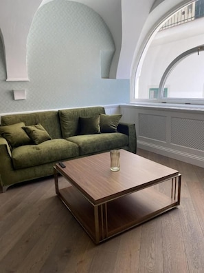 Una stanza con un divano verde, un tavolino in legno e un'ampia finestra ad arco.