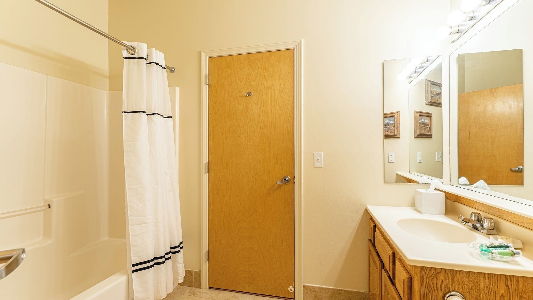 A bathroom with a wooden door, a white shower curtain, a sink with a mirror, and a towel rack.