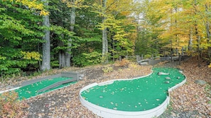 Un campo de mini golf con superficie de césped verde, rodeado de árboles y una valla de madera.