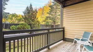 Une véranda couverte avec une balustrade, deux chaises et une vue sur les arbres et une clôture.