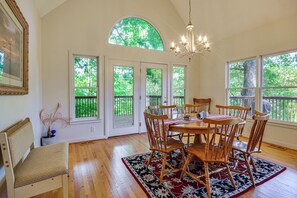 A dining room with a chandelier, wooden chairs, a table, and large windows with a view of greenery. - Pinnacle Lakefront Retreat: Dock, Canoe & Fire Pit (Pinnacle)