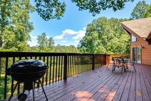 A wooden deck with a barbecue grill, outdoor furniture, and a view of a forested area. - Pinnacle Lakefront Retreat: Dock, Canoe & Fire Pit (Pinnacle)