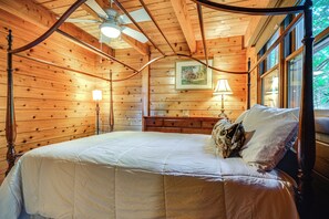 Een slaapkamer in een houten chalet met een hemelbed, twee bedlampen en een plafondventilator.