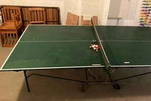 A ping pong table with a net in the center, surrounded by wooden chairs.