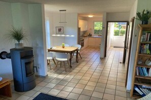 A spacious living area with a central table, a built-in wood stove, and a kitchen in the background.