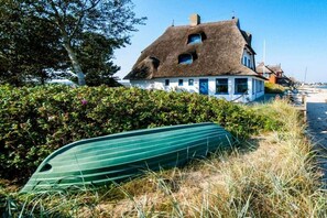 A traditional thatched-roof house with a white facade, a green boat on the grass, and a clear sky.