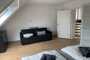 Ein modernes Zimmer mit einem schwarzen Sofa, einem Bett mit weißer Bettwäsche und Holzboden.