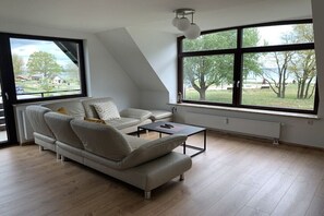 Ein modernes Wohnzimmer mit einem Ecksofa, einem Couchtisch und großen Fenstern mit Blick ins Freie.