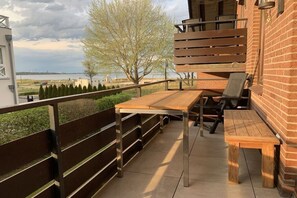 Un patio al aire libre con una mesa y sillas de madera, una barandilla de metal y vistas al mar.