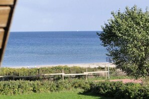 A beach view with a clear sky, a distant sailboat, and a sign indicating a nearby restroom. - Baltic Sea Dream Kronsgaard (Kronsgaard)