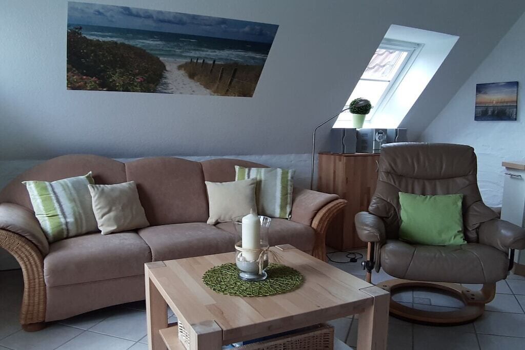 Un salon comprenant un canapé, un fauteuil inclinable, une table basse et un tableau représentant une plage.