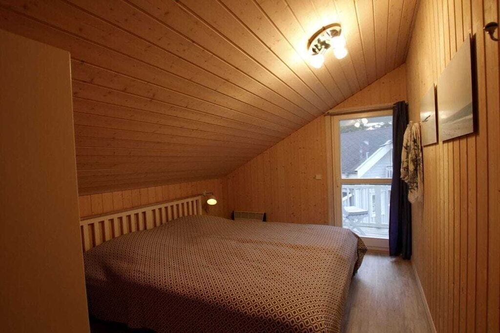 A bedroom with a sloped ceiling, a bed, a window, and a radiator.