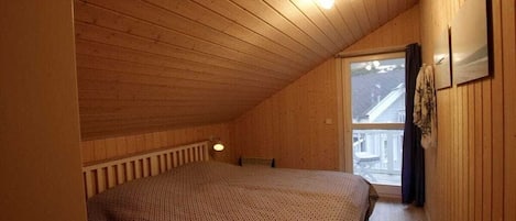 A bedroom with a sloped ceiling, a bed, a window, and a radiator.