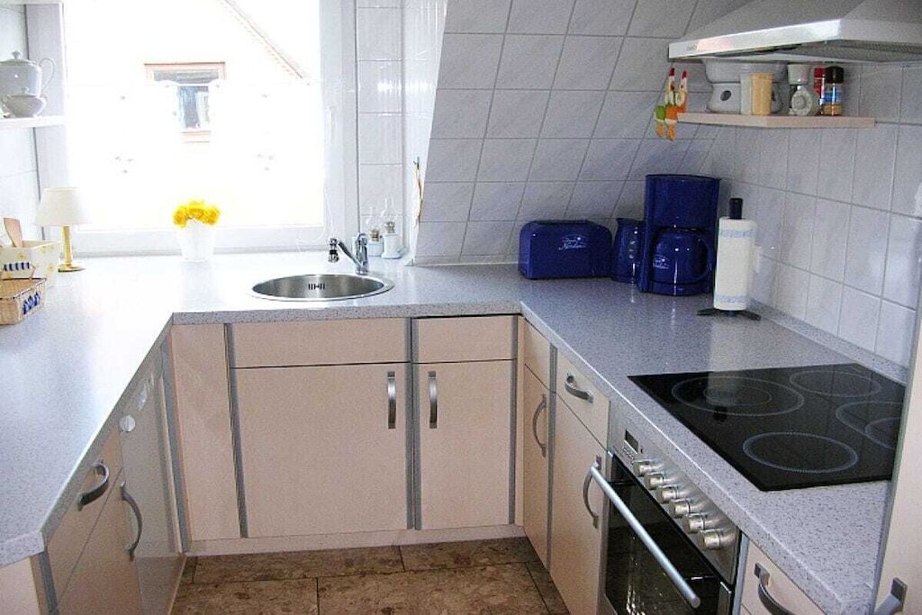 Une cuisine équipée d’un évier, d’une cuisinière, de placards et d’une fenêtre agrémentée de fleurs.