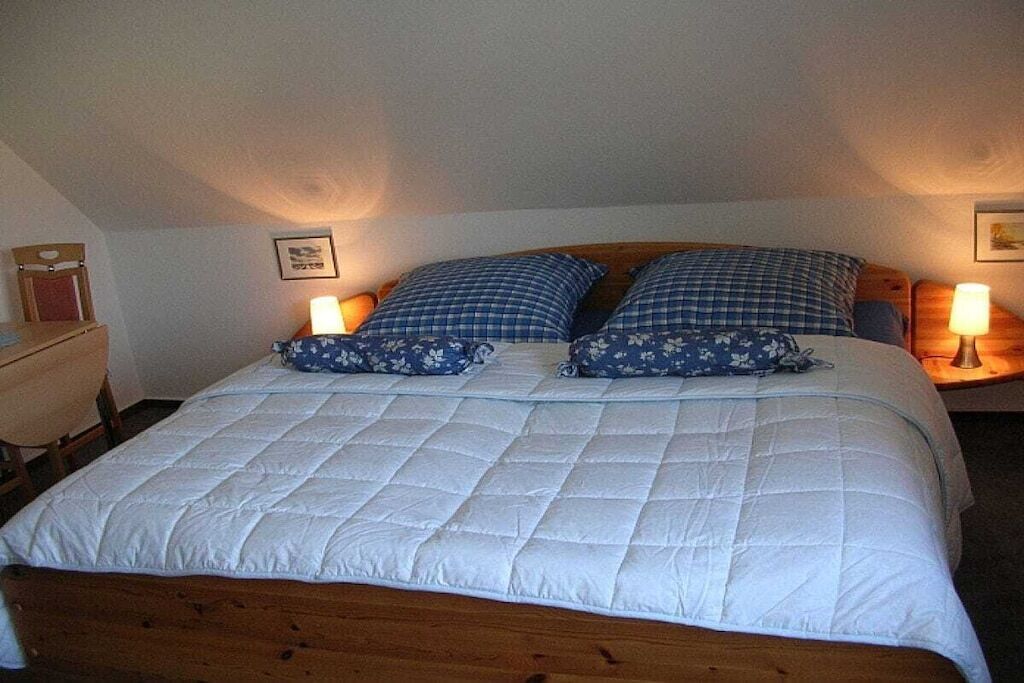 A single bed with a white quilted bedspread and two blue floral pillows. There are two bedside lamps on either side of the bed.