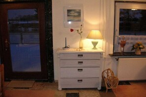 Quarto com cômoda branca, abajur, vaso com flor, quadro na parede e janela com vista.