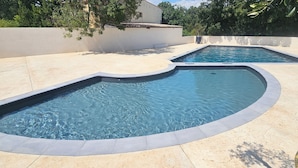 Duas piscinas com bordas curvas, rodeadas por um deck ladrilhado e um muro baixo.
