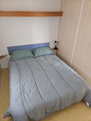 A bed with a blue headboard, a bedside table with a lamp, and a wall-mounted power outlet. - 4-person mobile home in PRL with a pool and access to the Ardèche (Pradons)