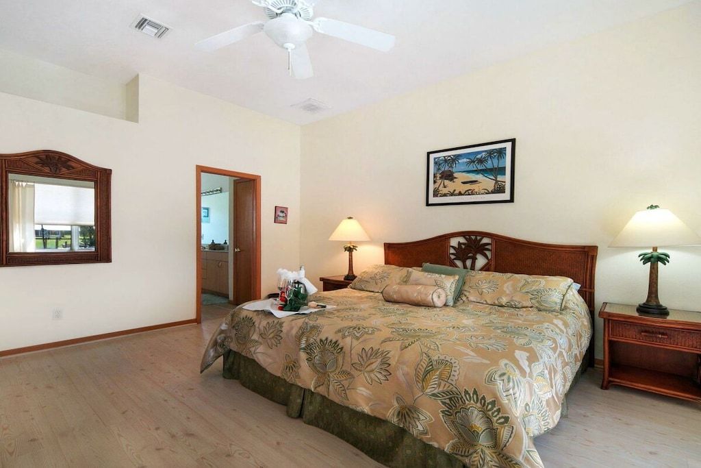Een slaapkamer met een bed, een plafondventilator, een nachtkastje, een lamp, een ingelijst schilderij aan de muur en een deur die naar een andere kamer leidt.