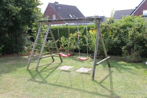 A wooden swing set in a backyard with a lawn and a hedge. - Holiday apartment with 2 bedrooms (Norden-Norddeich)