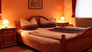 Una cama de madera con cabecera, dos mesitas de noche con lámparas, una colcha y un cuadro enmarcado en la pared.