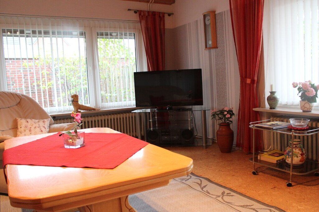 Un salon comprenant un téléviseur, un canapé, une table à manger avec un set de table rouge, un radiateur et une fenêtre avec des rideaux.