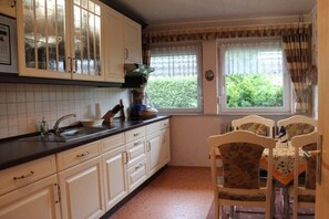 A kitchen with white cabinets, a black countertop, and a window with curtains. - Holiday apartment with 2 bedrooms (Norden-Norddeich)
