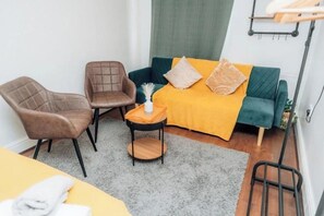 A room with a bed, two chairs, a small table with a vase, and a hanging rack. - Stylish Brick Lane Apartment | Sleeps 6 (London)