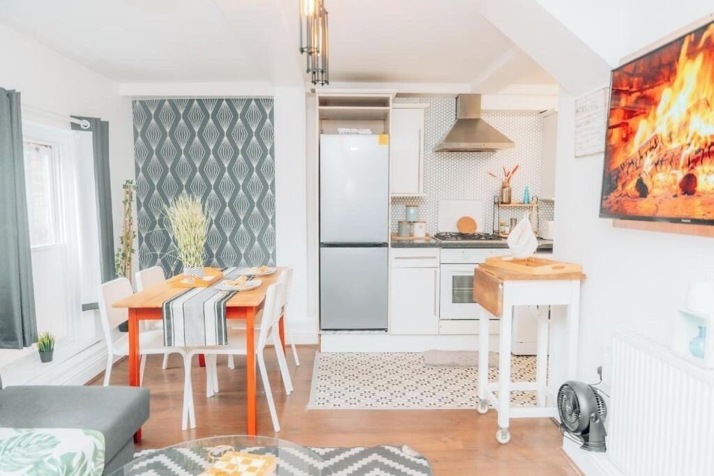 Eine moderne Küche mit weißen Schränken, einem Edelstahl-Kühlschrank und einem Essbereich mit Holztisch und Stühlen.
