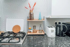 Une cuisine équipée d’une cuisinière à gaz, d’un grille-pain, d’une machine à café et d’une étagère contenant des ustensiles de cuisine.