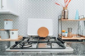 A kitchen with a gas stove, a hexagonal patterned backsplash, and a shelf with kitchen items. - Stylish Brick Lane Apartment | Sleeps 6 (London)