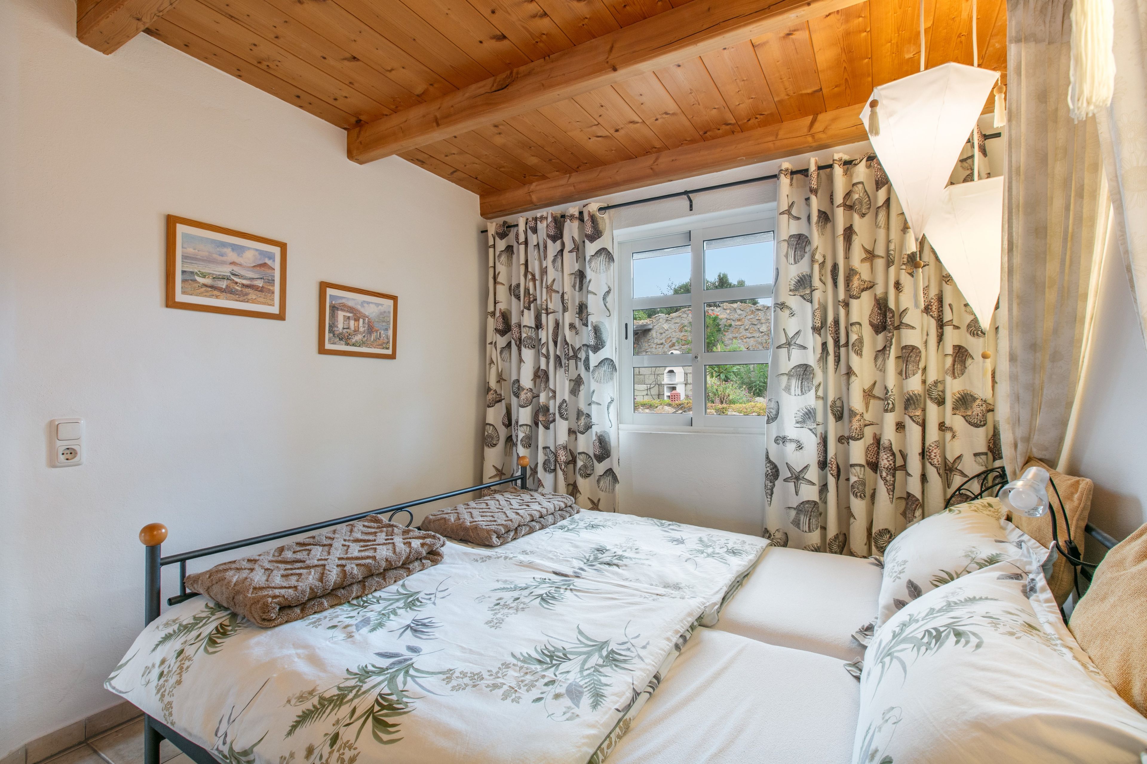 A bedroom with a bed, a window with curtains, and two framed pictures on the wall.