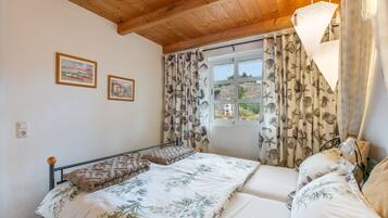 A bedroom with a bed, a window with curtains, and two framed pictures on the wall.