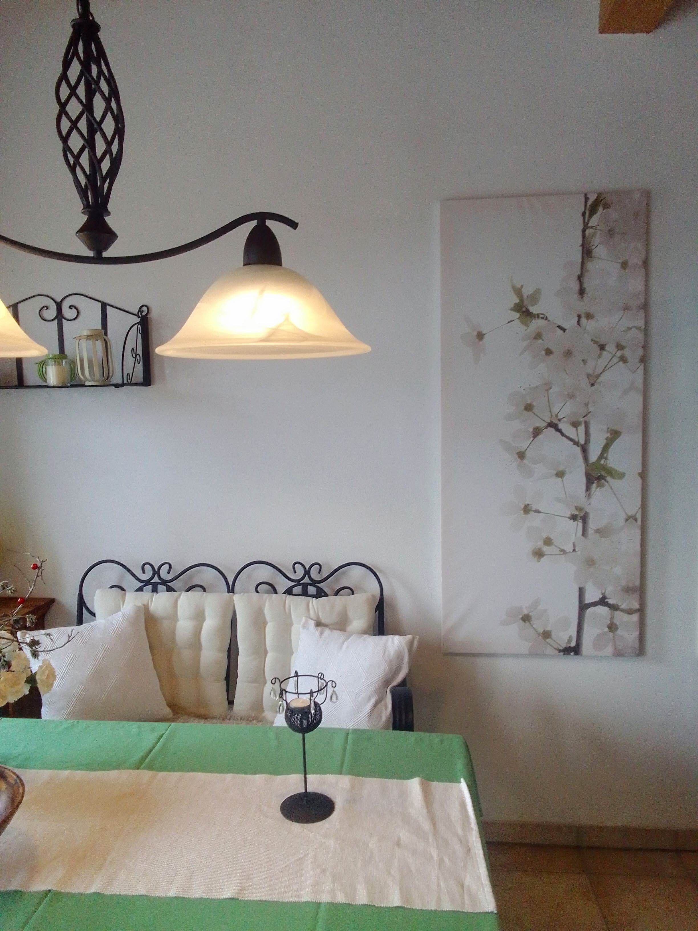 A room with a bed, a hanging lamp, a wall-mounted shelf, and a large floral painting.