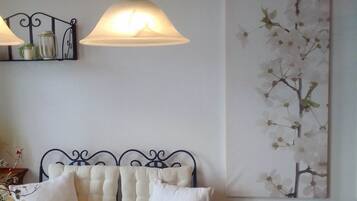 A room with a bed, a hanging lamp, a wall-mounted shelf, and a large floral painting.