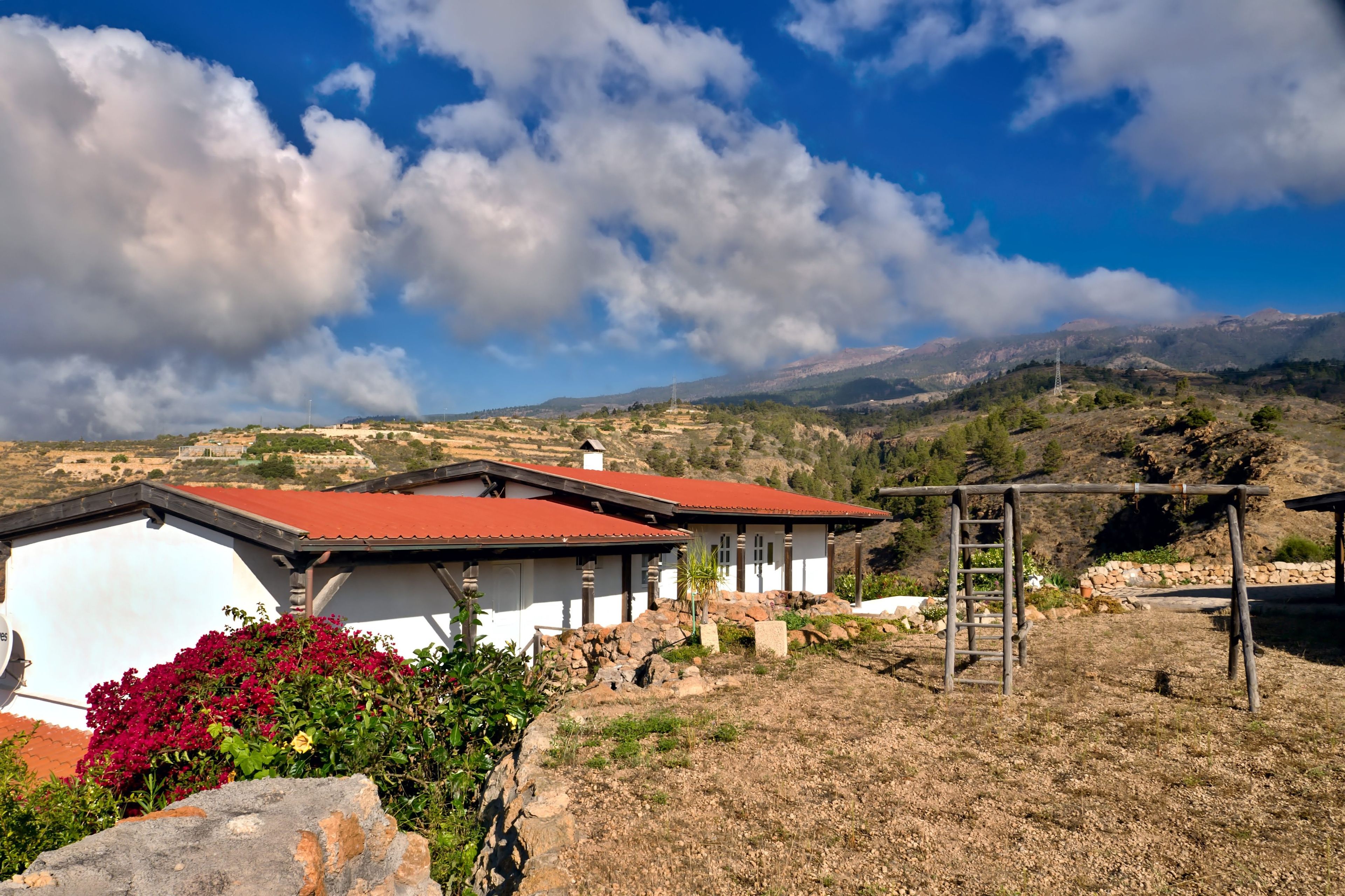 A rural house with a red roof, surrounded by dry grass and a stone wall.