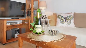 Een woonkamer met een houten salontafel, een fles wijn, een televisie en een bank met een kussen in de vorm van een vlinder.